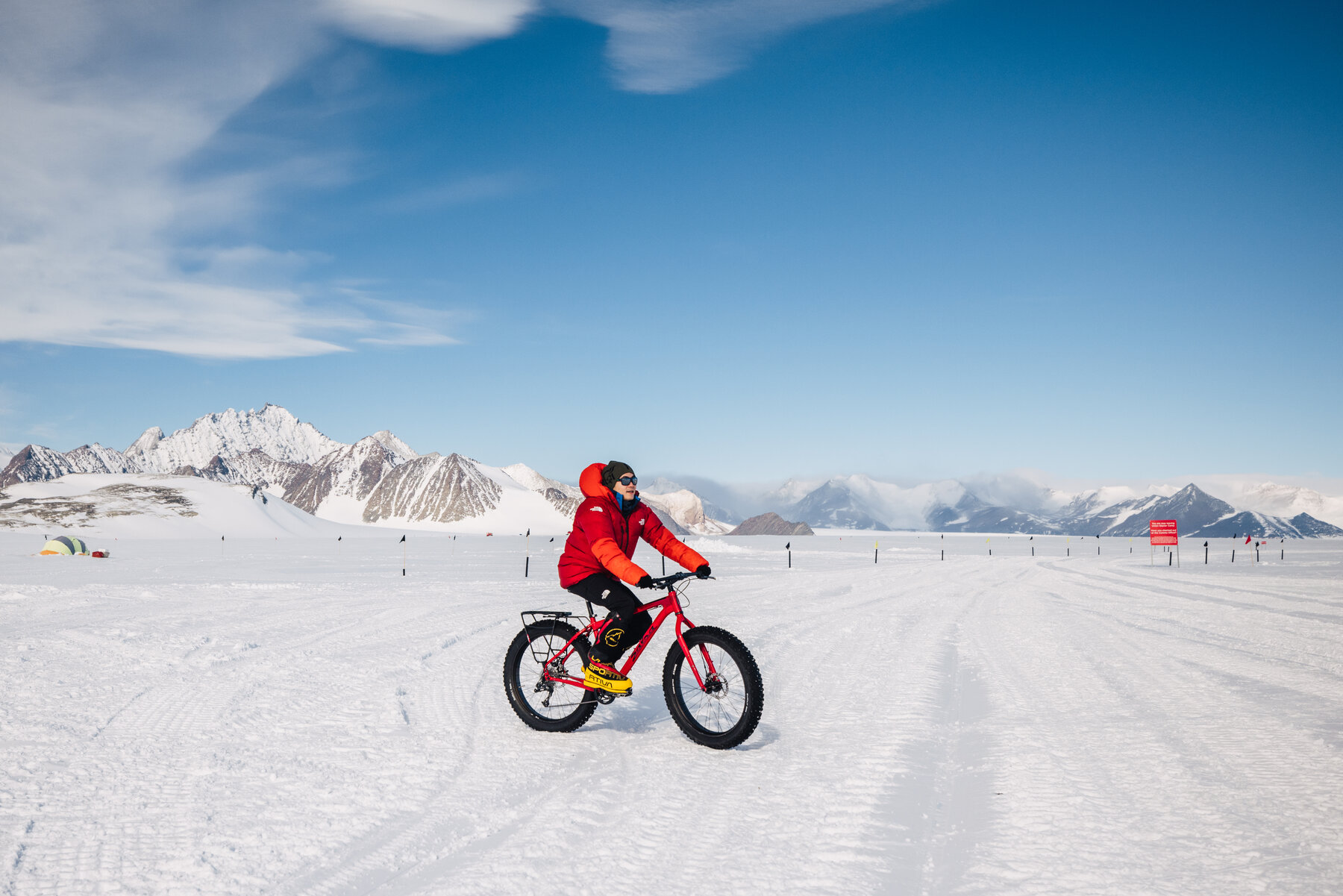 Person riding a fat tire bike across the Union Glacier ice with Antarctic mountains behind