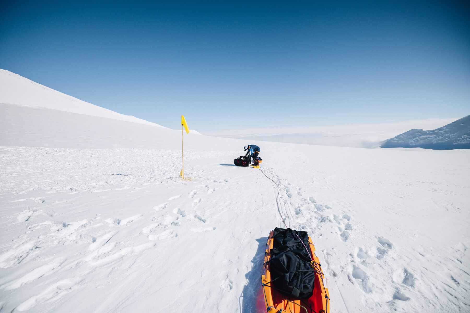 Climber hauling a sled past a marker wand on the glacier route to Low Camp