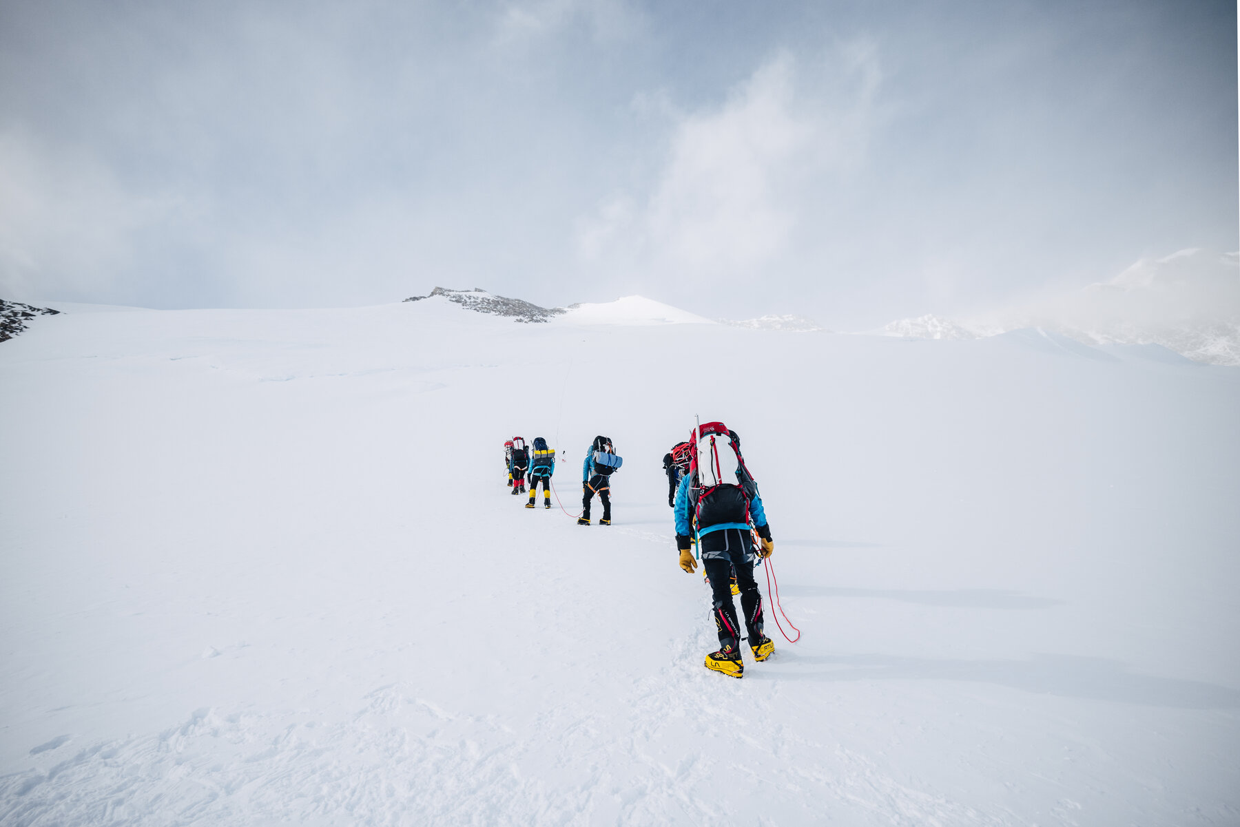 Team of roped climbers with packs walking up the snow slope at the start of the west face route