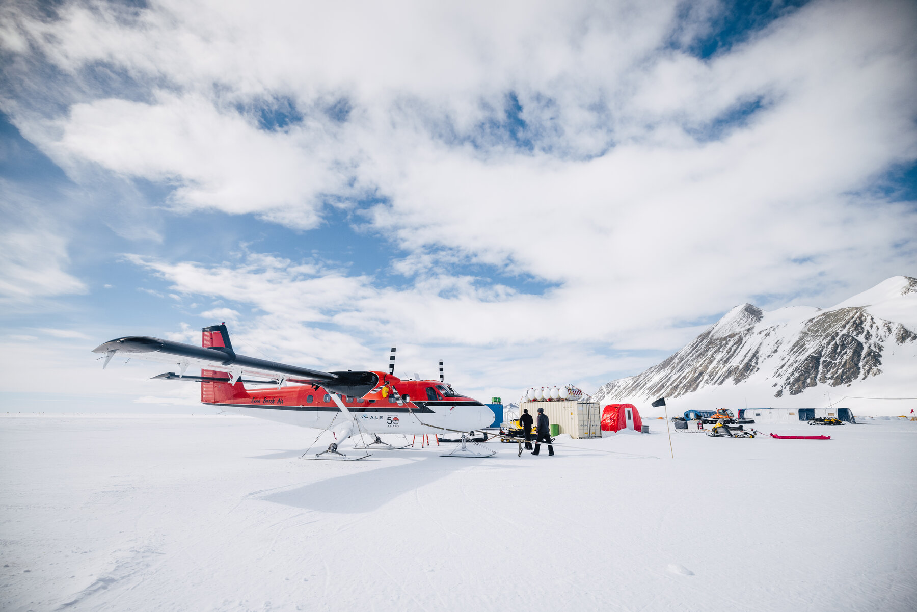 Red Twin Otter ski plane parked on the snow at Vinson Base Camp with mountains behind