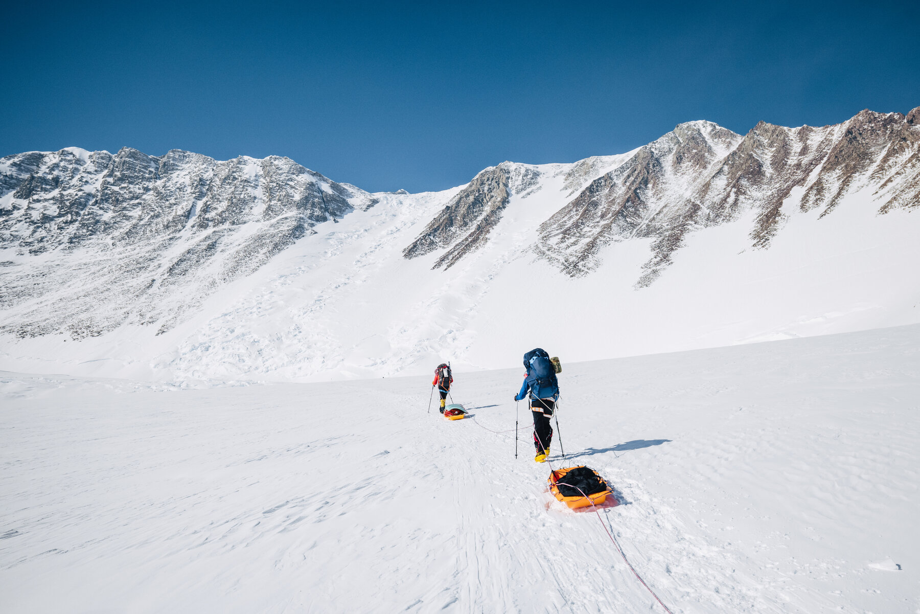 Two climbers pulling sleds up a glacier slope with the Ellsworth Mountains behind