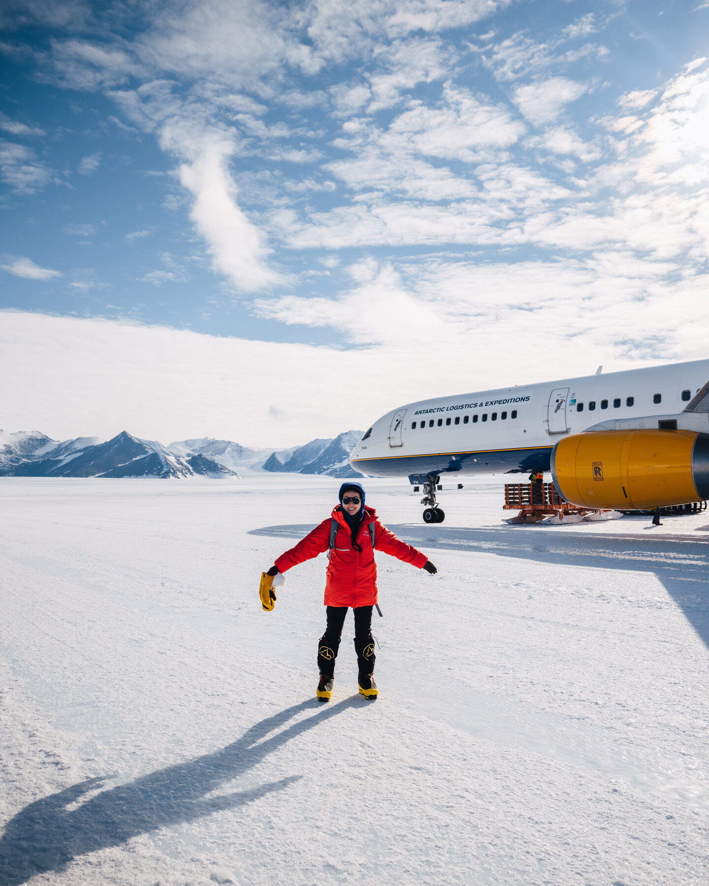 Person with arms spread on the Union Glacier ice runway in front of the charter plane