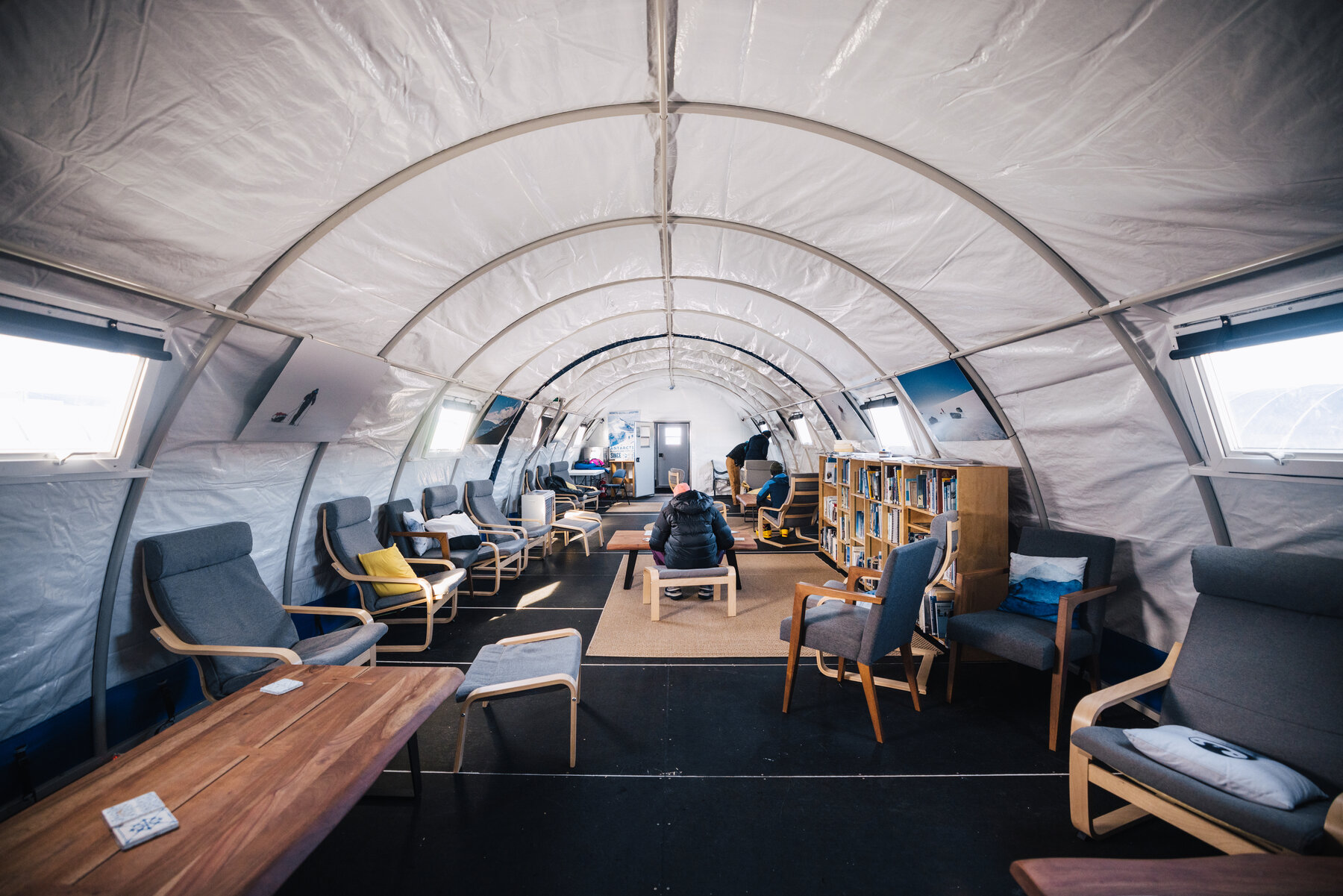 Interior of the Union Glacier Camp lounge tent with armchairs, bookshelves and a long table under the arched roof