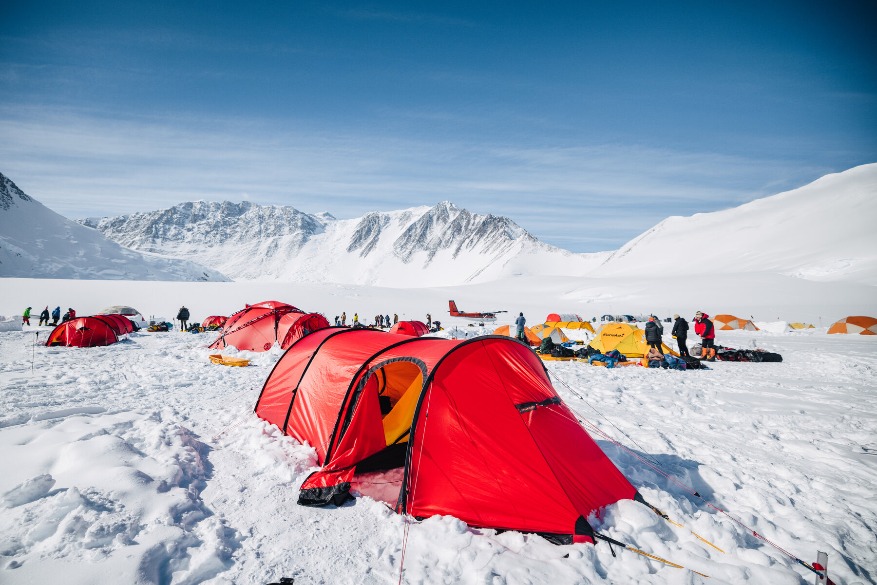 Red expedition tents at Vinson Base Camp with ski plane and mountains behind